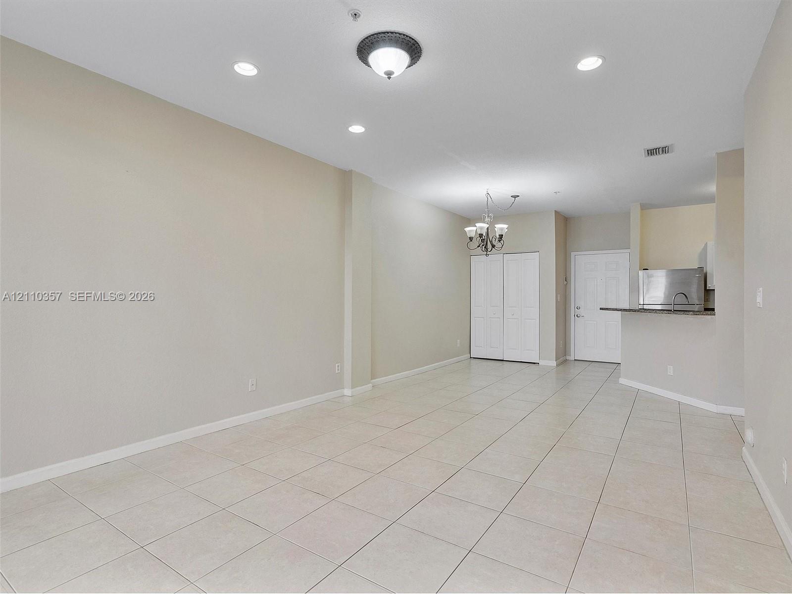 Open floor plan featuring neutral-tone tile flooring, recessed lighting, a multi-arm chandelier, and a breakfast bar with stone-surface countertop