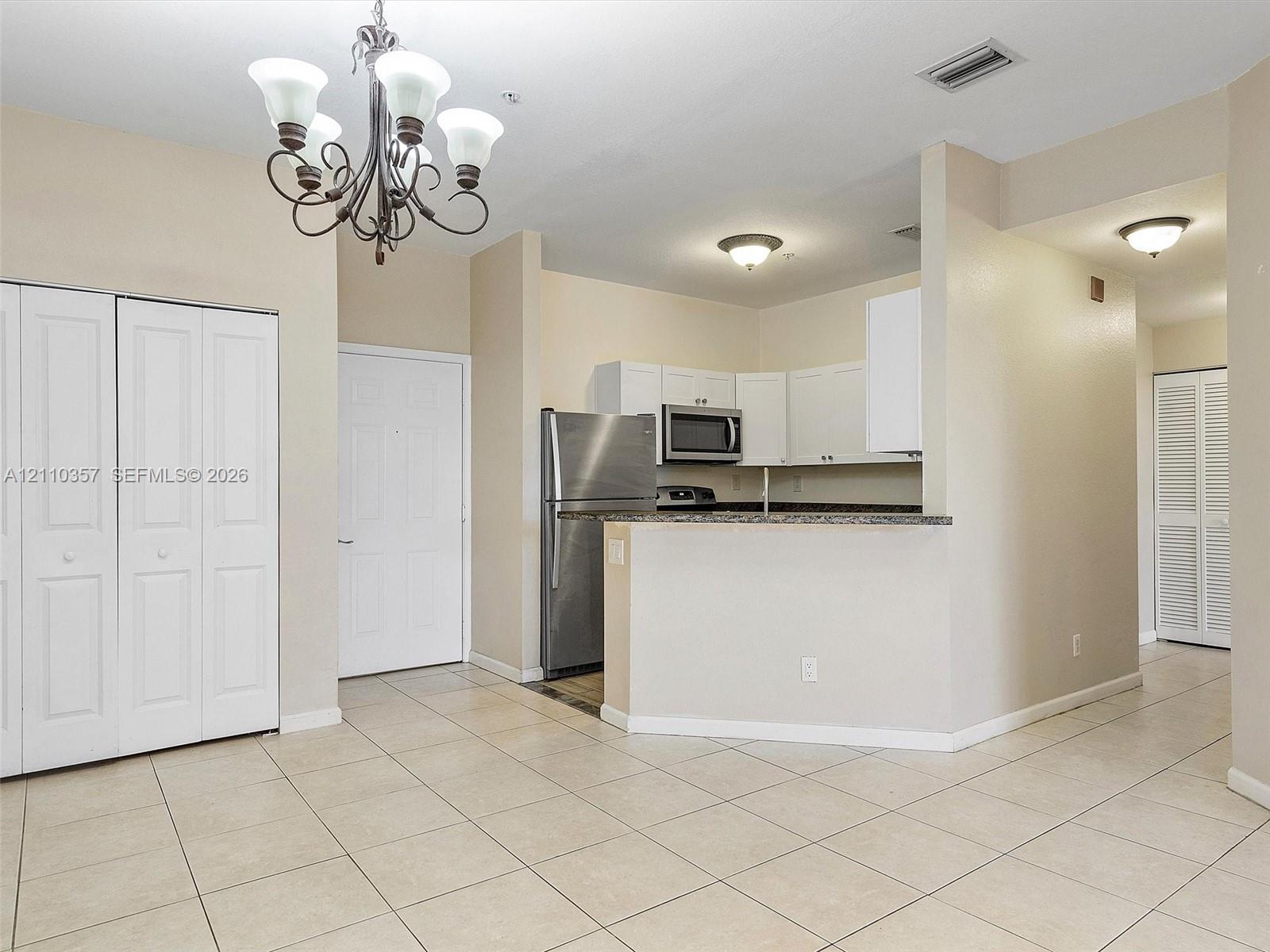 Kitchen featuring white cabinetry, stone-finish countertops, stainless steel refrigerator, and built-in microwave, accented by a decorative multi-arm chandelier and tile flooring