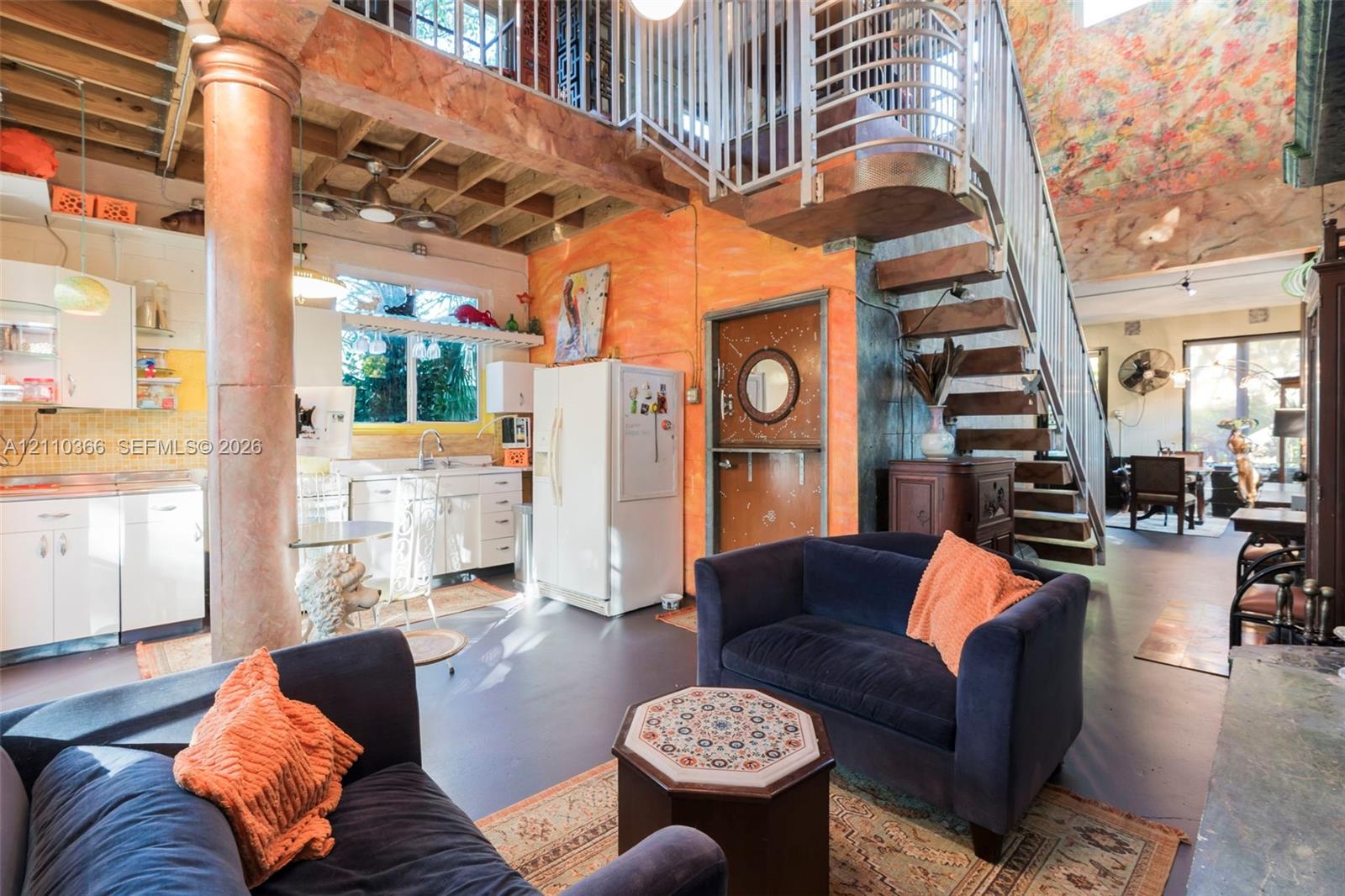 Open-concept interior featuring a structural support column, exposed ceiling joists, a metal staircase with a matching railing, and a Dutch-style door with a circular window