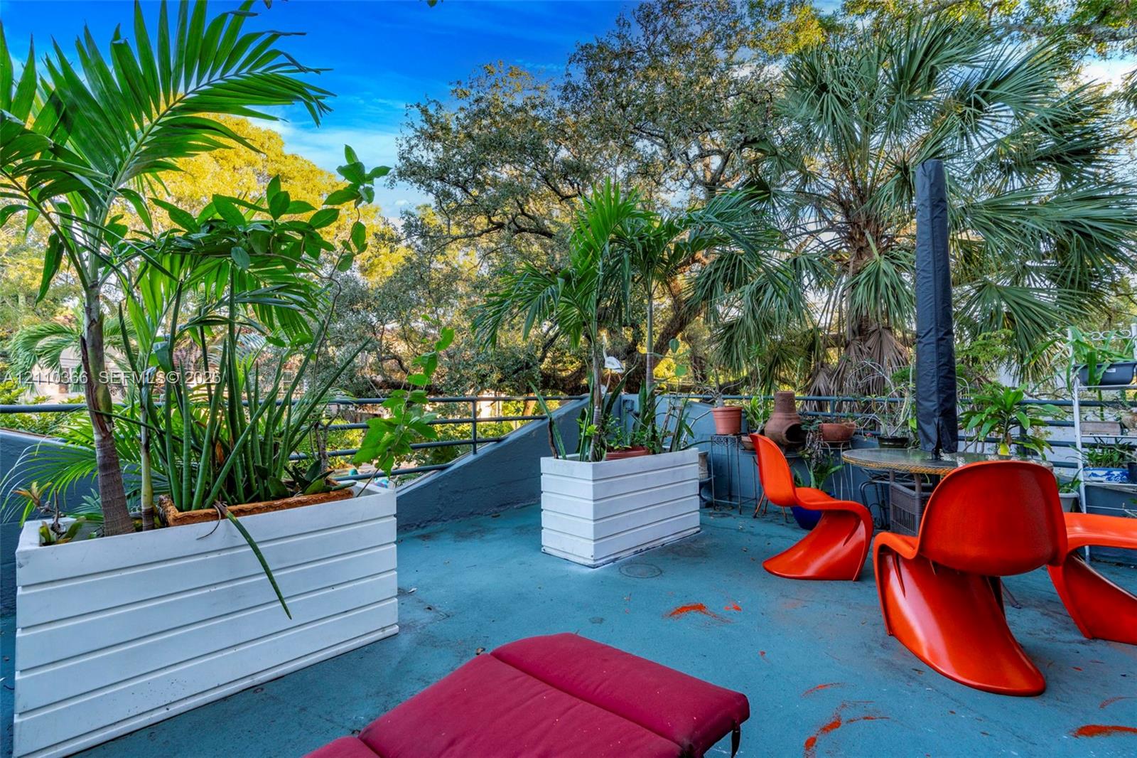 Rooftop terrace featuring white horizontal-slat planters, mature trees, and metal railing