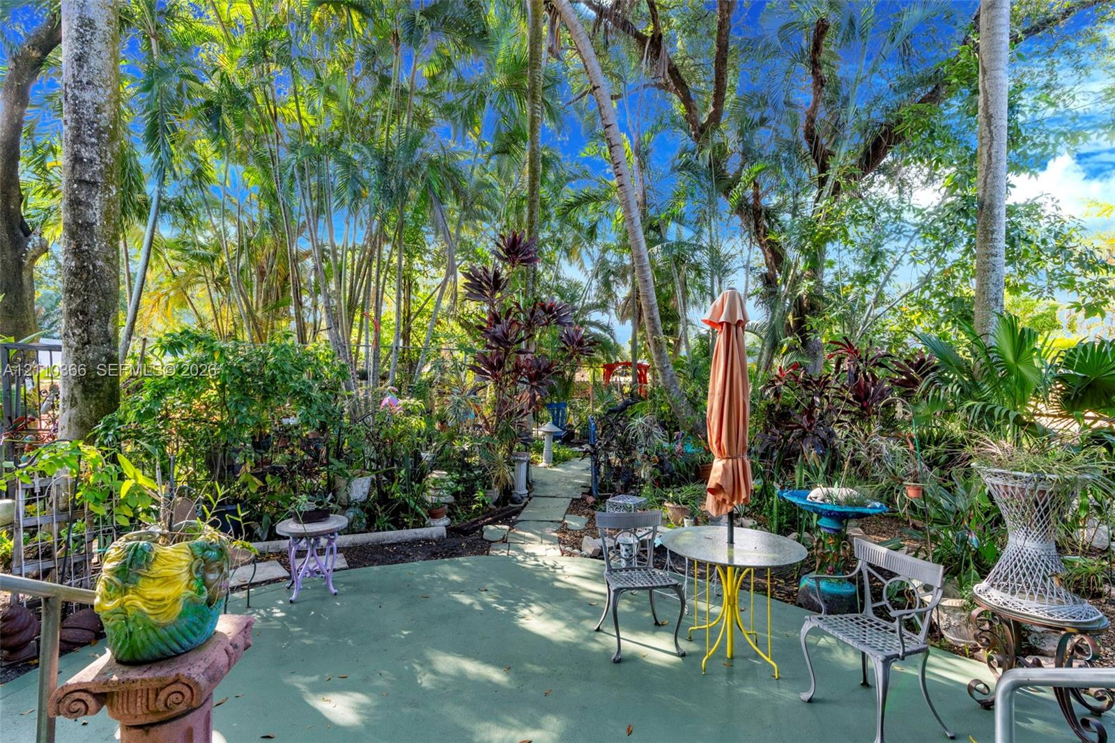 Rear outdoor patio featuring a concrete surface and natural stone paver pathway surrounded by mature trees and lush tropical vegetation
