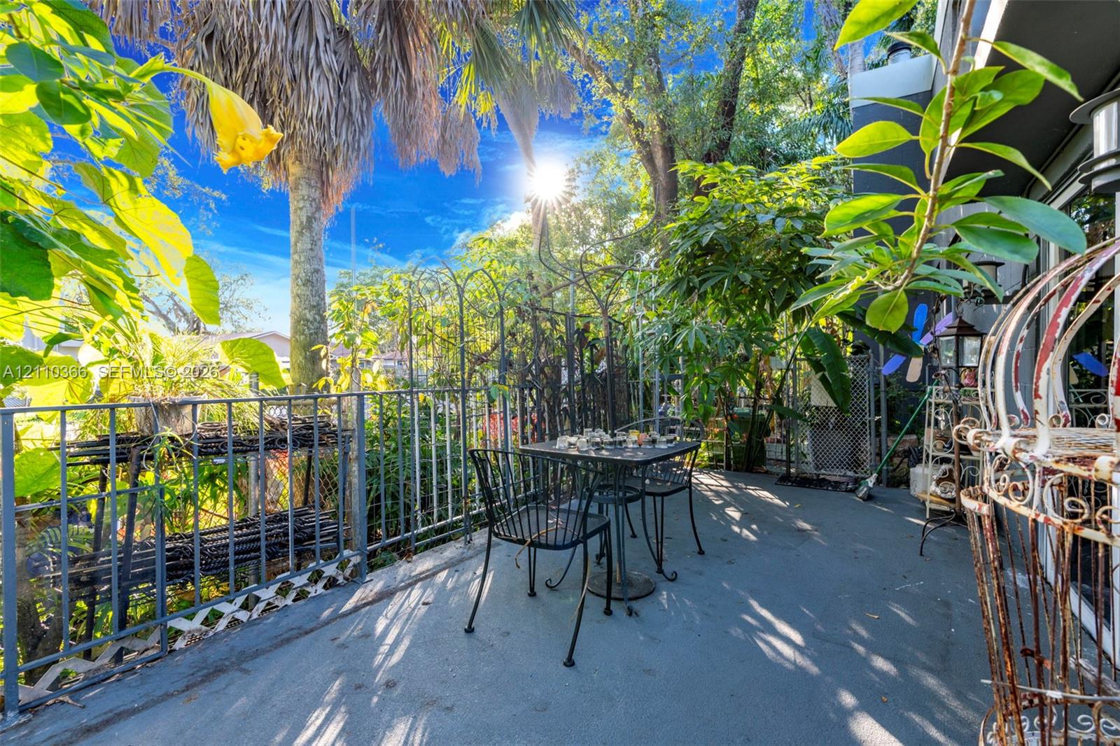 Outdoor patio featuring a concrete floor, decorative metal perimeter fencing, and mature landscaping