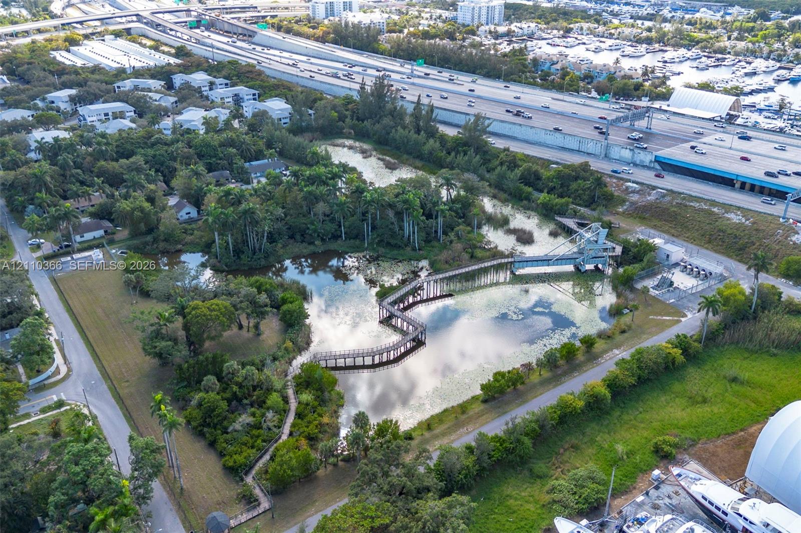 Expansive grounds featuring a natural pond, mature tropical vegetation, a winding wooden pedestrian boardwalk, and a raised metal observation structure