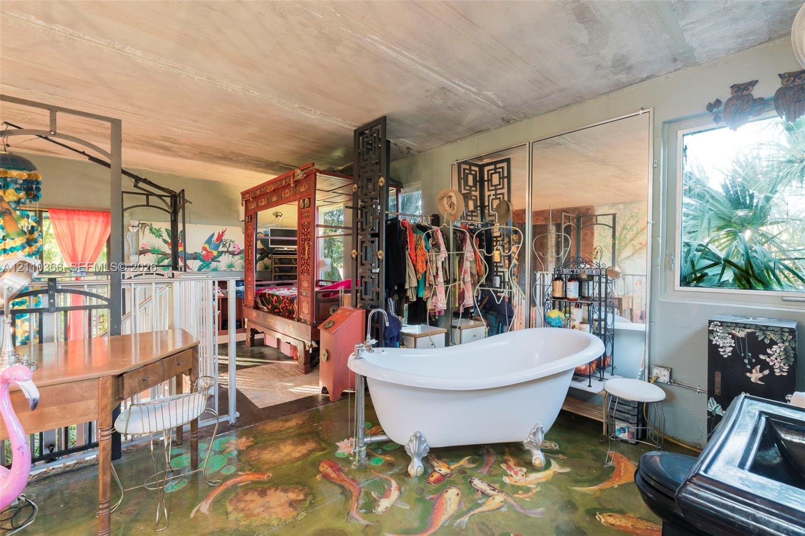 Freestanding clawfoot soaking tub with a floor-mounted faucet, expansive mirrored wall panels, and stained concrete flooring with decorative artistic detailing