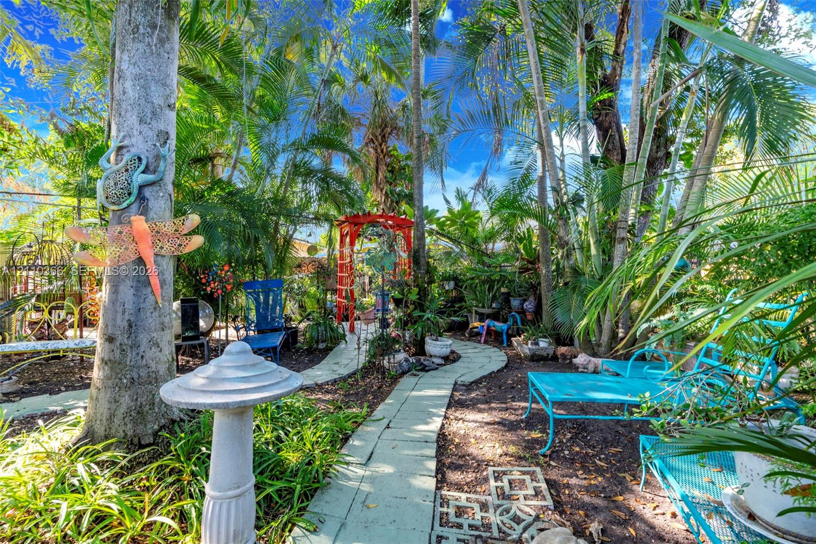 Landscaped grounds featuring mature palm trees, a concrete paver walkway, and a decorative metal garden arch