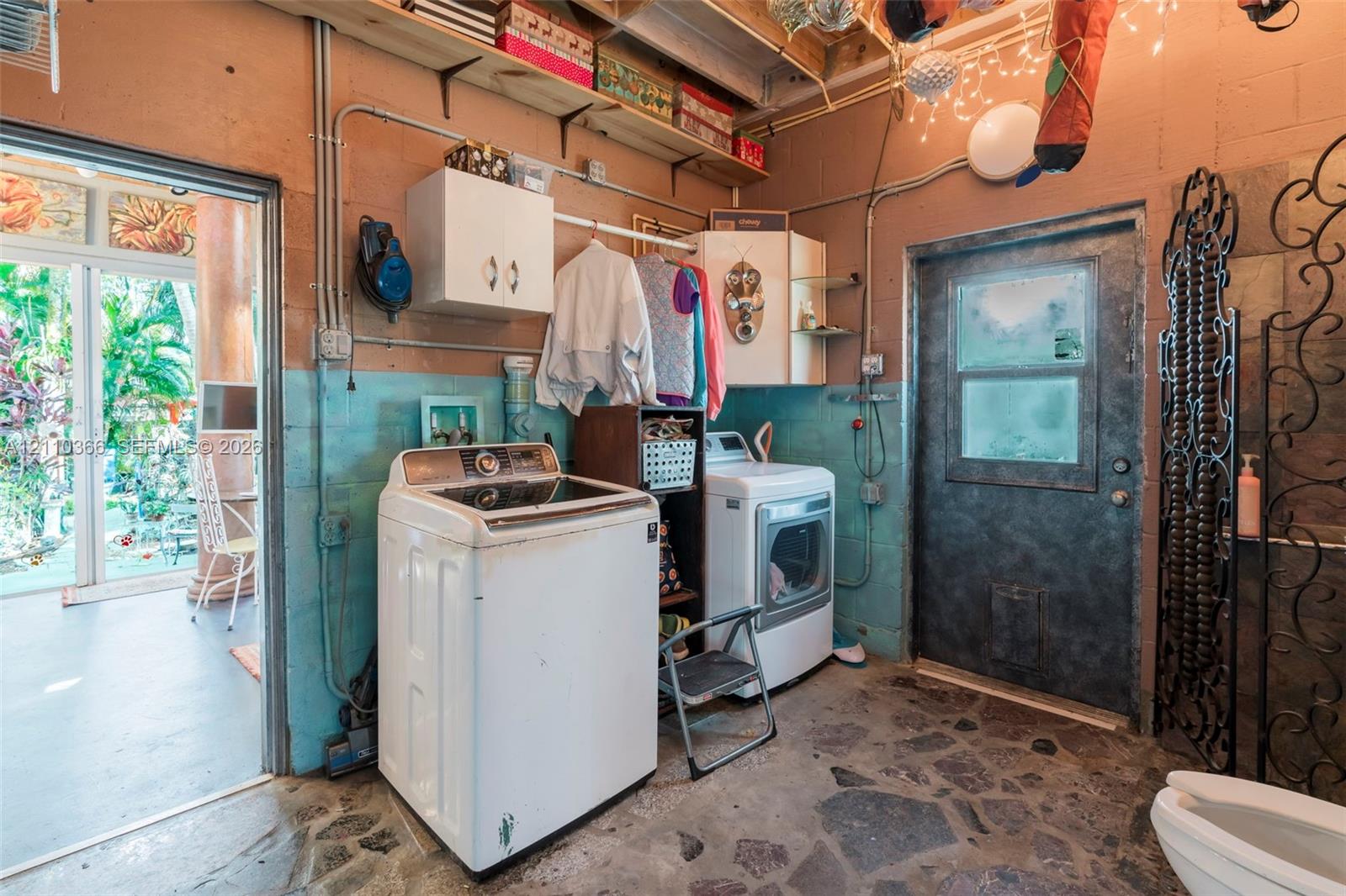 Utility room featuring slate-patterned stone flooring, dual-tone painted masonry walls, integrated wall-mounted storage cabinetry, and a glass-paneled exterior entry door