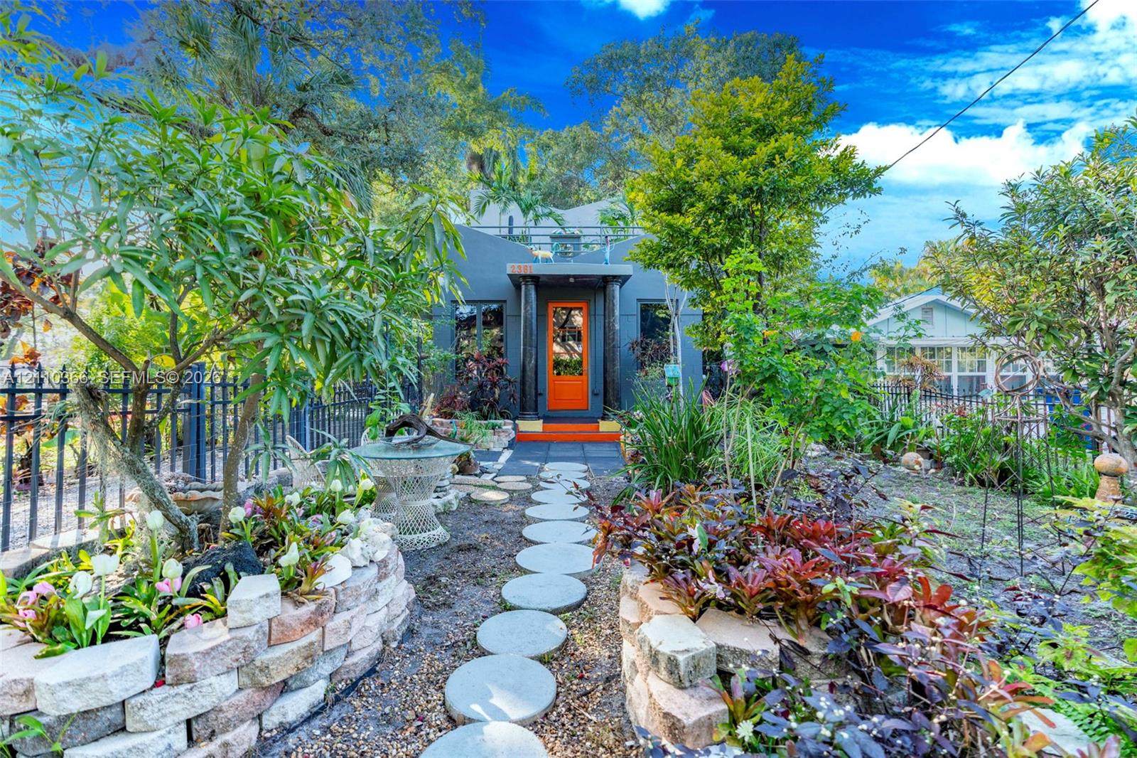 Exterior facade featuring a bold orange front door, columns, flat roofline, stone-finished raised planter beds, and a circular paver walkway