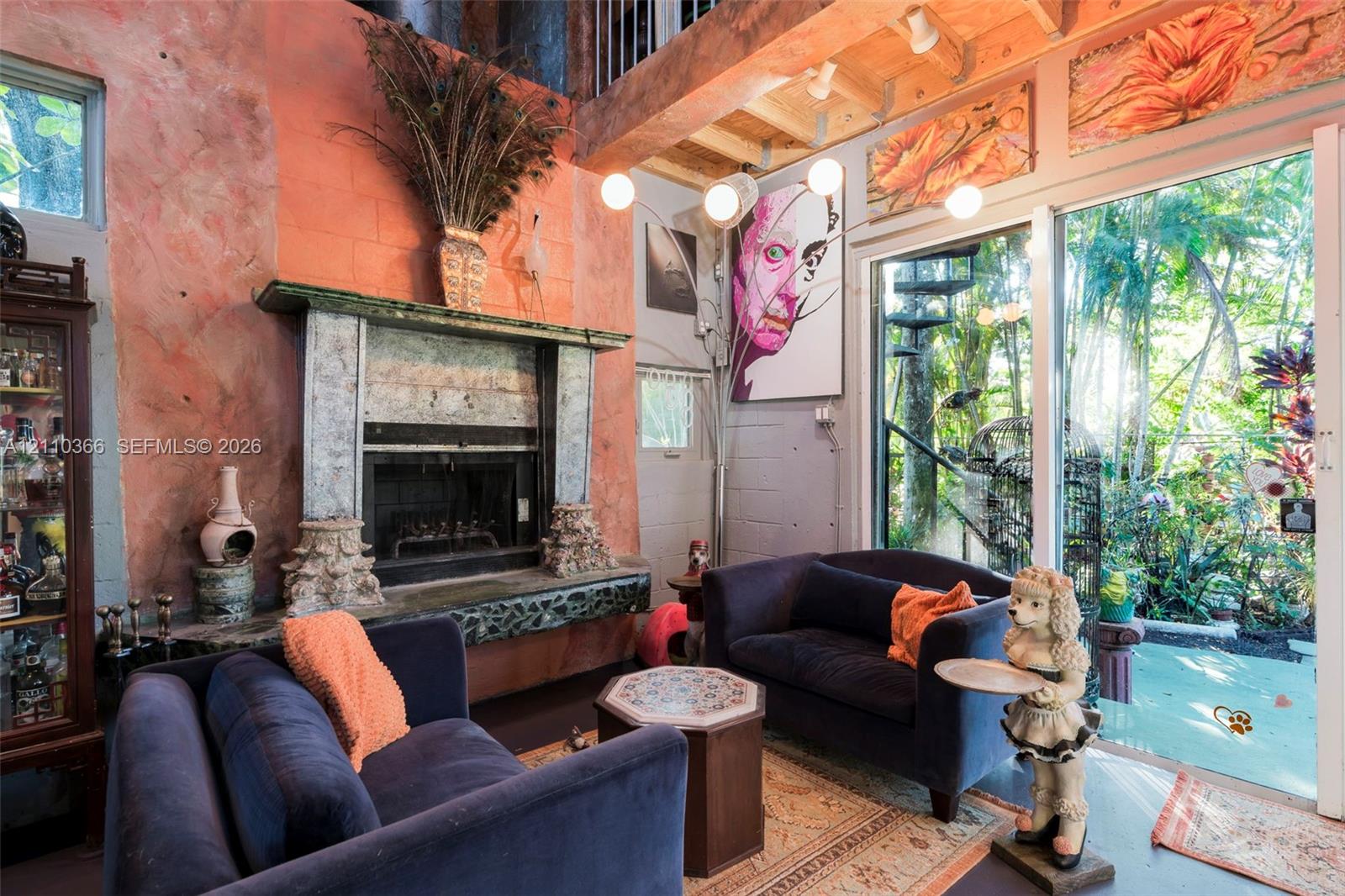 Double-height living area featuring an exposed wood-beam ceiling, textured coral-toned wall, fireplace with an ornate stone mantel, and floor-to-ceiling glass sliding doors