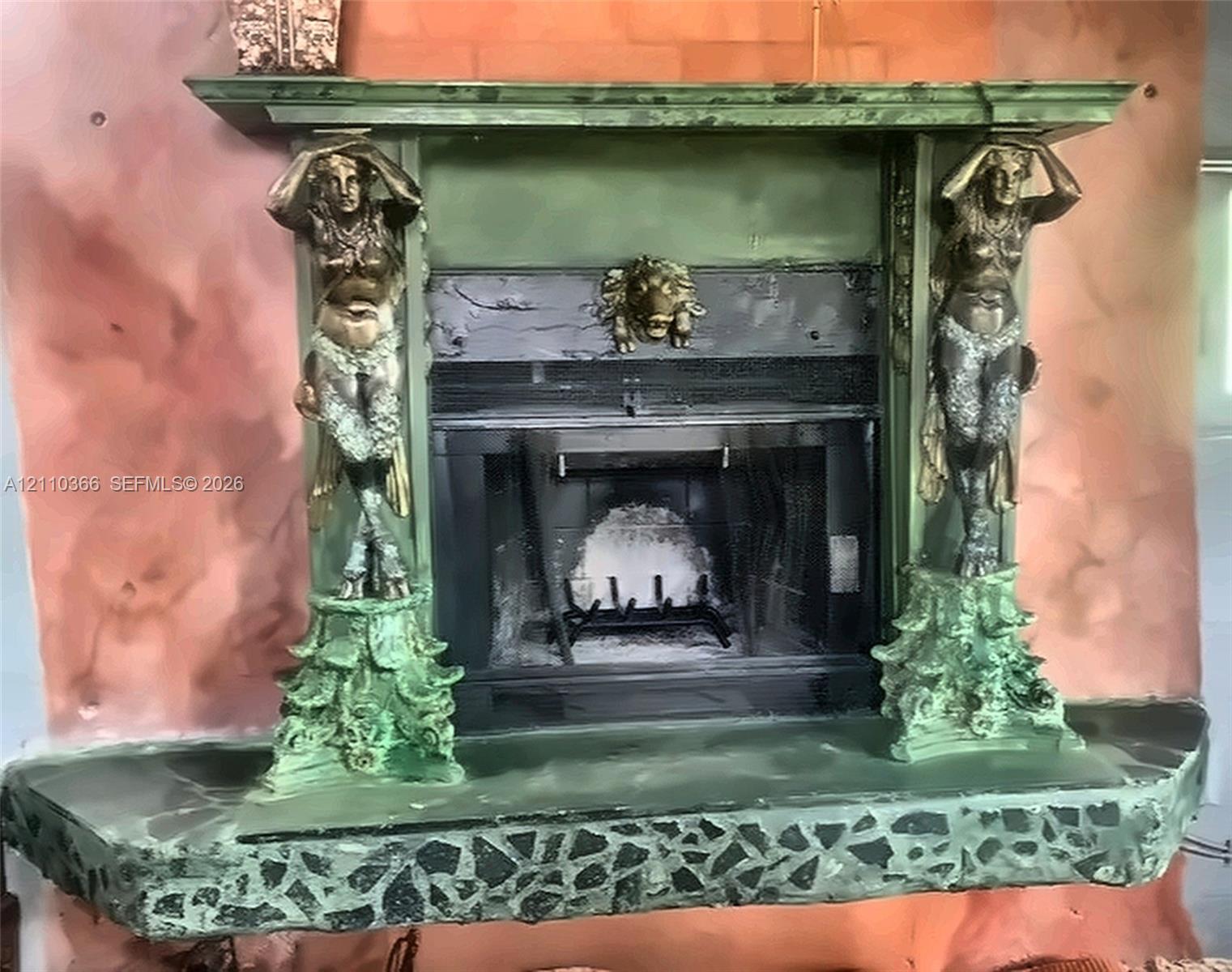 Fireplace with a custom mantle featuring dual caryatid supports, a central lion-head relief, and an integrated stone-composite hearth