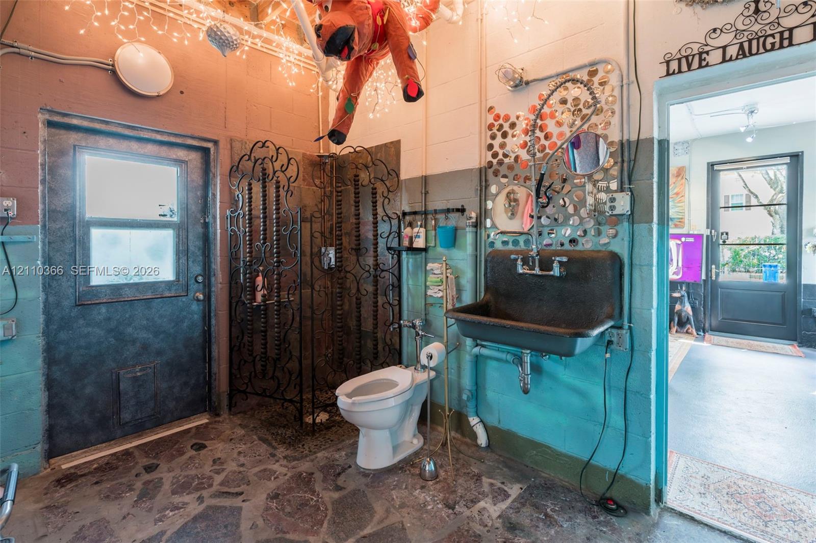 Industrial-style space featuring a wall-mounted utility sink, metal-framed walk-in shower enclosure, floor-to-ceiling concrete block walls, and flagstone flooring