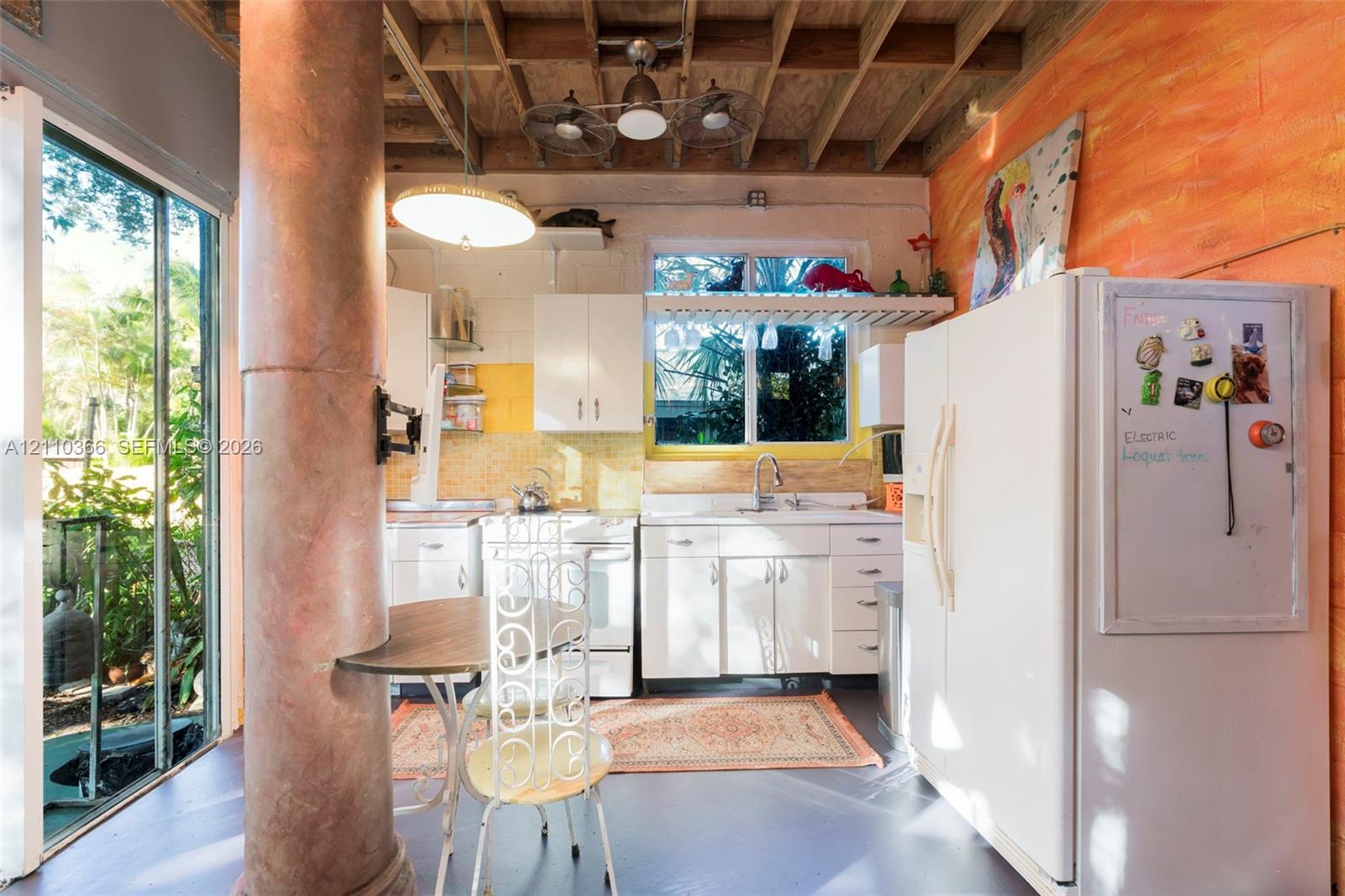 Kitchen featuring white cabinetry, an exposed beam ceiling, a structural support column, and floor-to-ceiling glass sliding doors