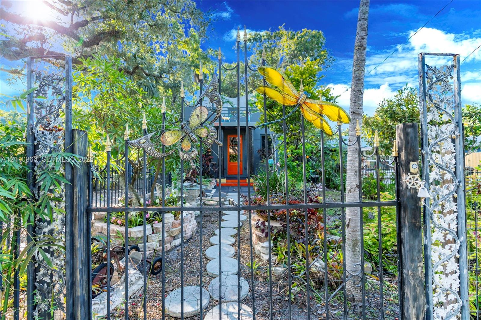 Custom metal gate featuring integrated insect-themed art, stone-paver walkway, and stone-retaining wall garden beds