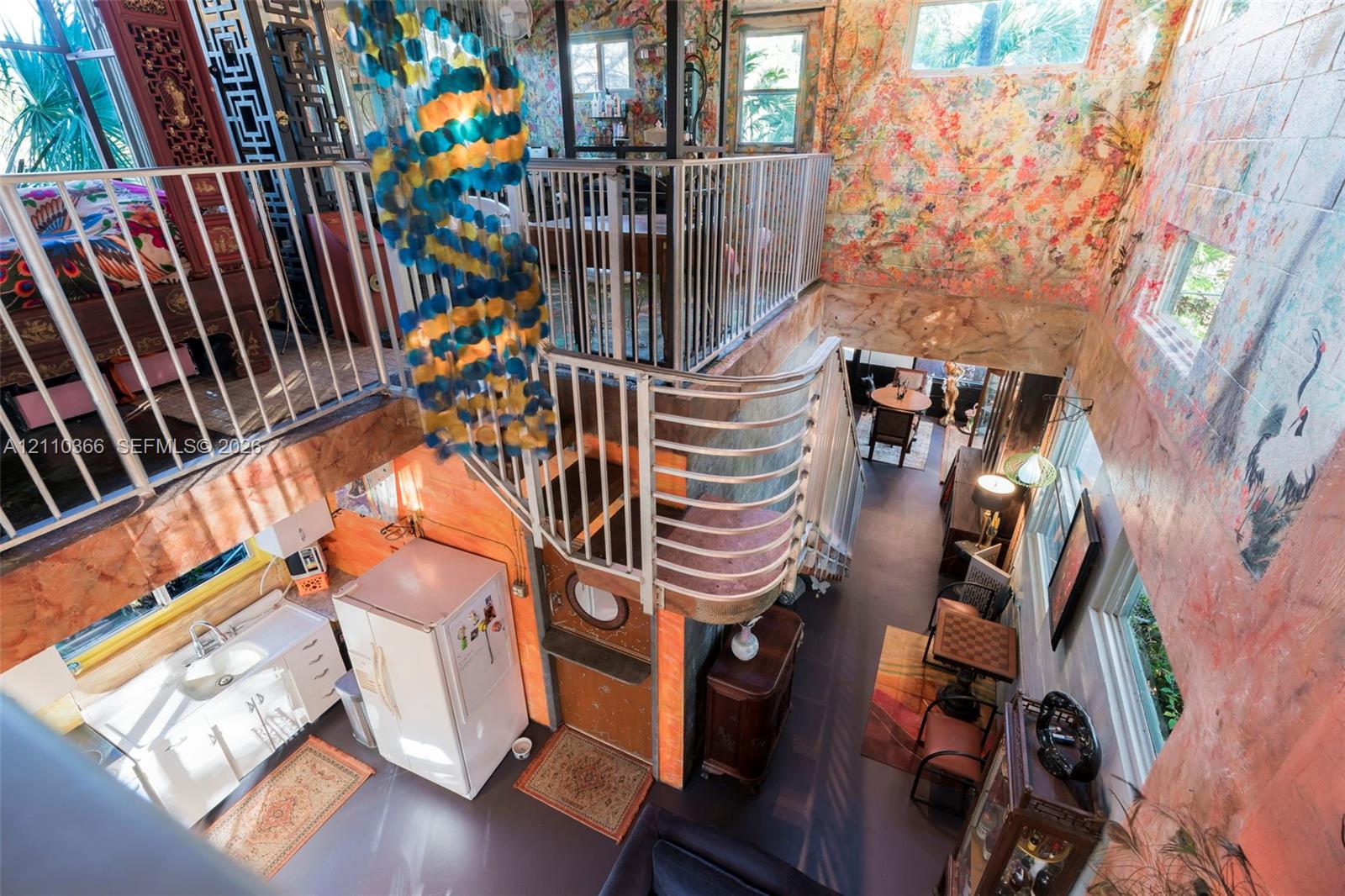 Multi-level interior featuring a mezzanine with metal railings, a curved staircase, floor-to-ceiling mural walls, and multiple clerestory windows