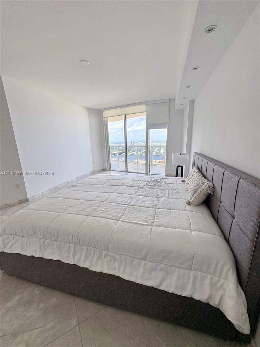 Floor-to-ceiling glass sliding doors opening to a balcony, polished stone-finish flooring, and recessed ceiling lighting