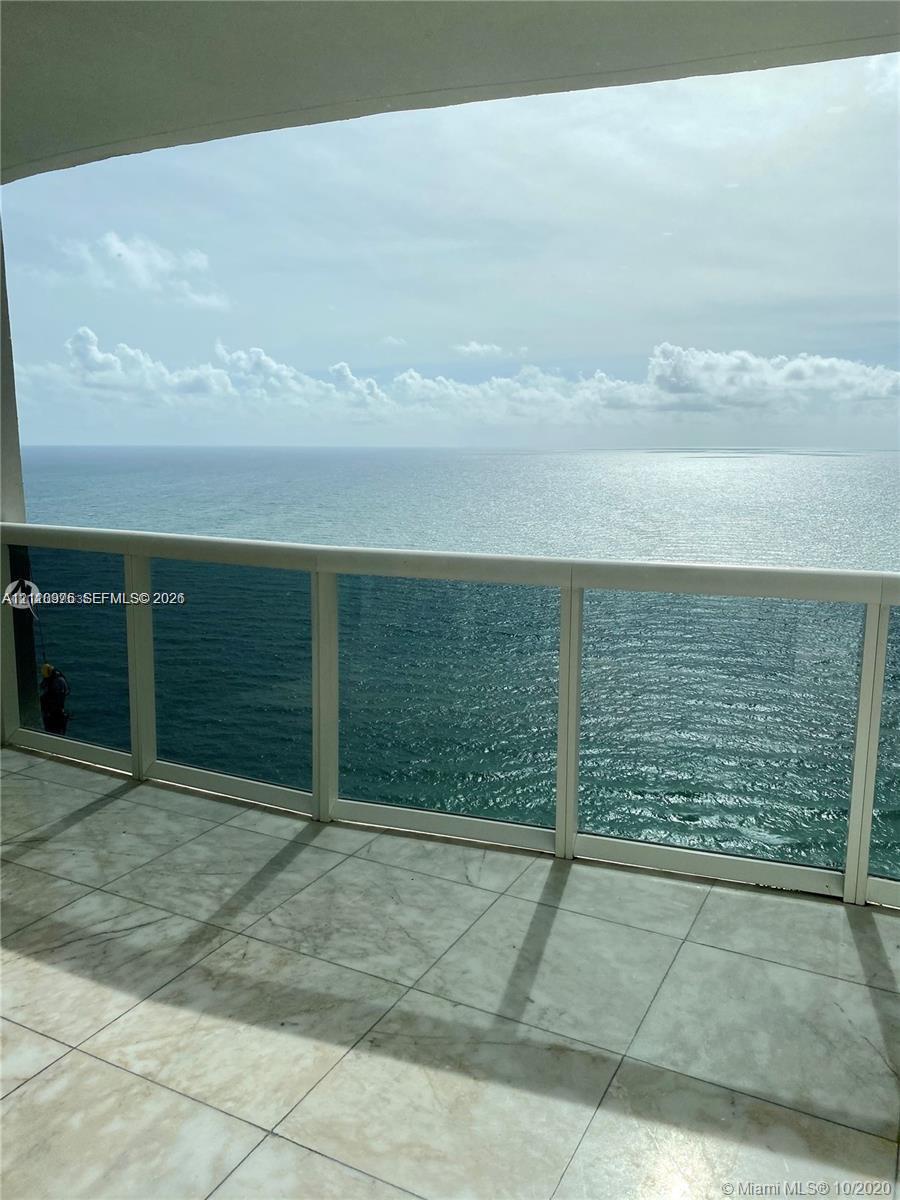Covered balcony featuring large-format tile flooring and a glass-paneled railing overlooking the ocean Covered balcony featuring large-format tile flooring and a glass-paneled railing overlooking the ocean