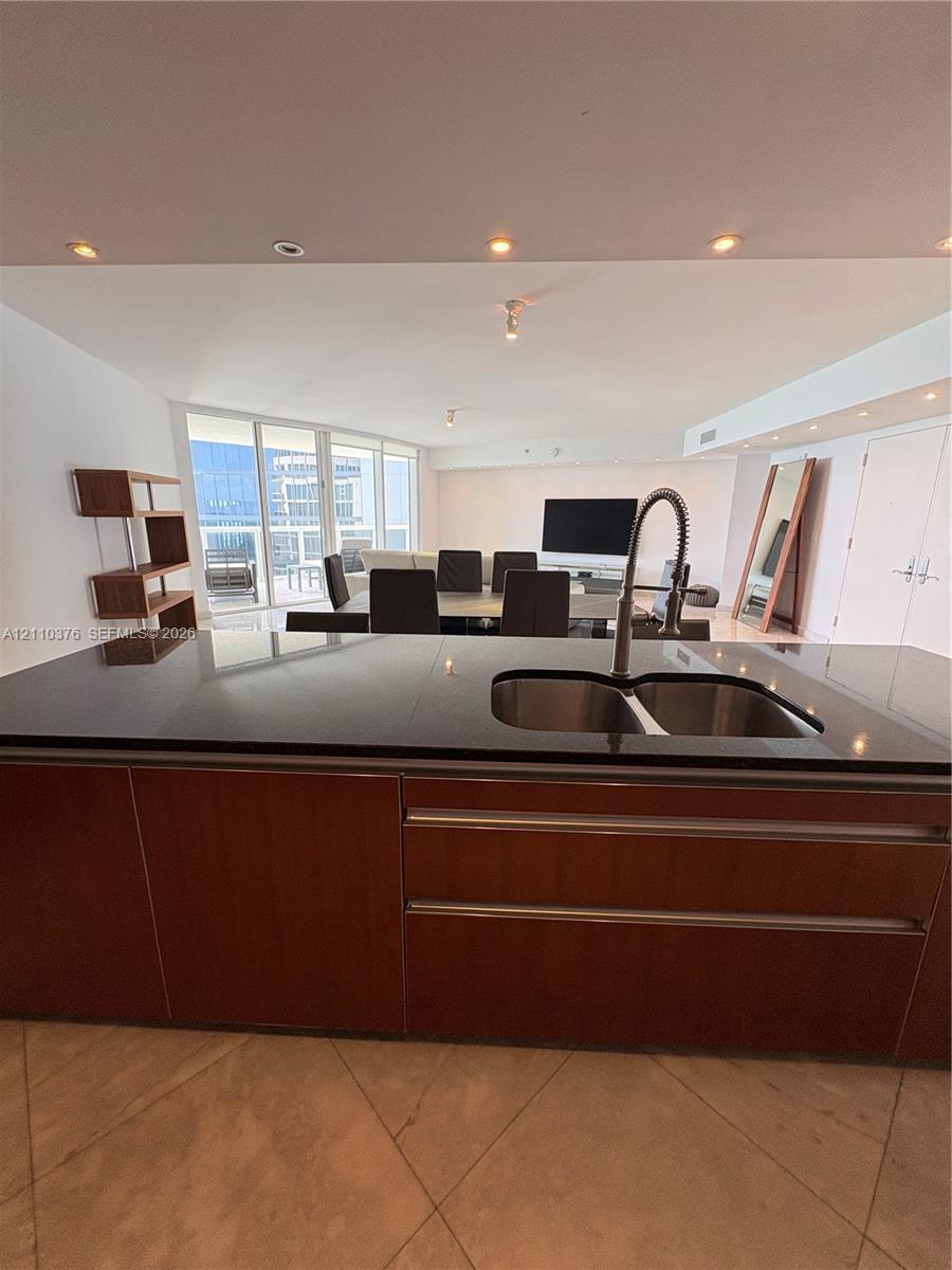 Kitchen island featuring dark-toned solid surfacing, stainless steel double-basin undermount sink, gooseneck faucet, and wood-finish cabinetry Kitchen island featuring dark-toned solid surfacing, stainless steel double-basin undermount sink, gooseneck faucet, and wood-finish cabinetry