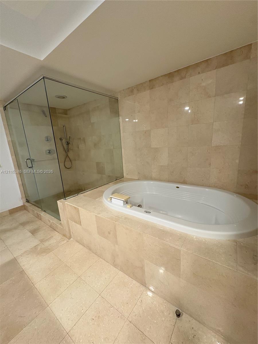 Bathroom featuring a deep soaking tub, separate glass-enclosed shower, and stone-tile wall and floor surfaces