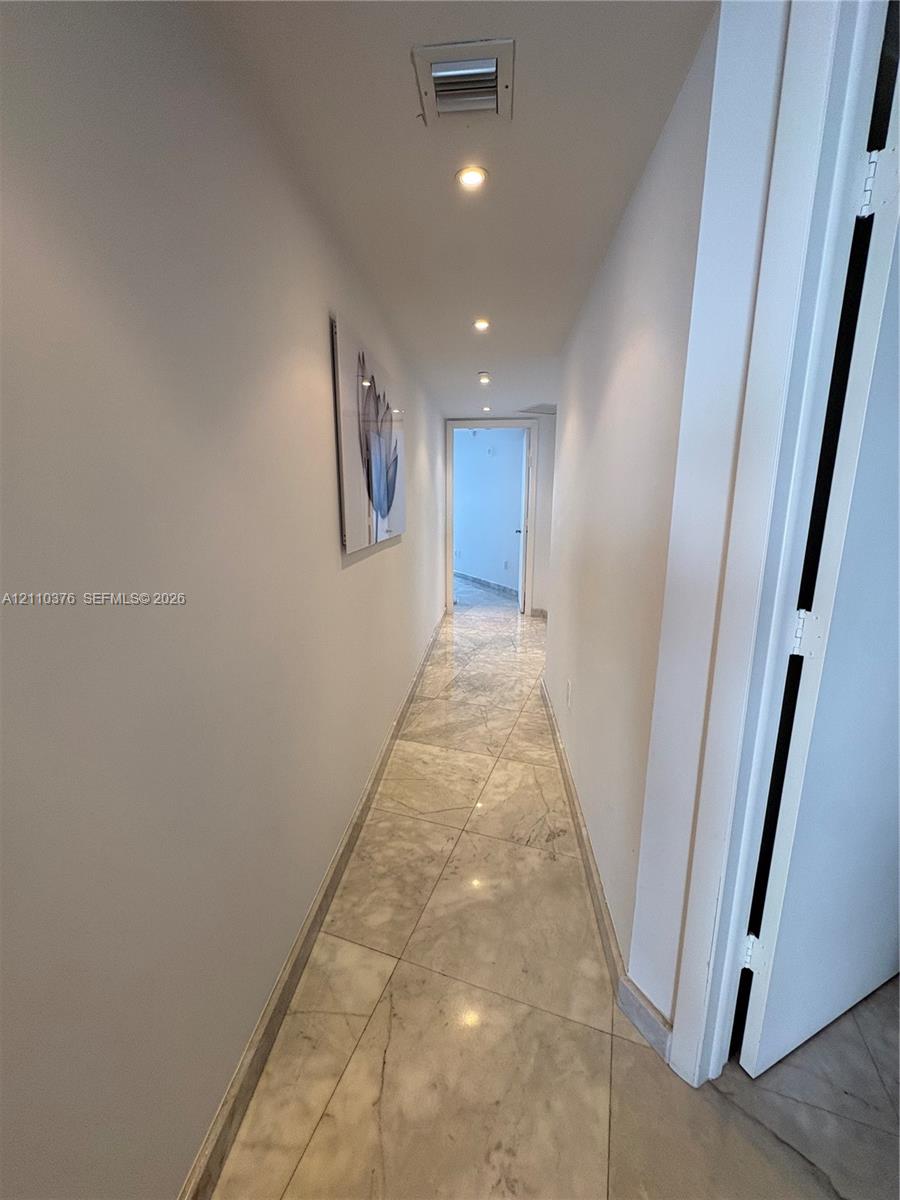 Hallway featuring large-format polished stone tile flooring and recessed ceiling lighting Hallway featuring large-format polished stone tile flooring and recessed ceiling lighting