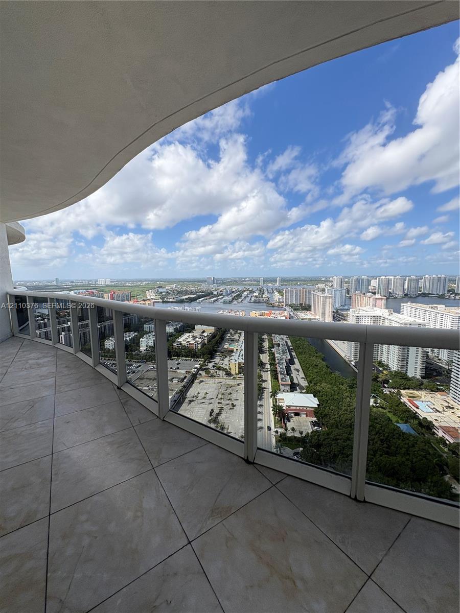 Covered private balcony featuring large-format tile flooring and floor-to-ceiling glass panel railings