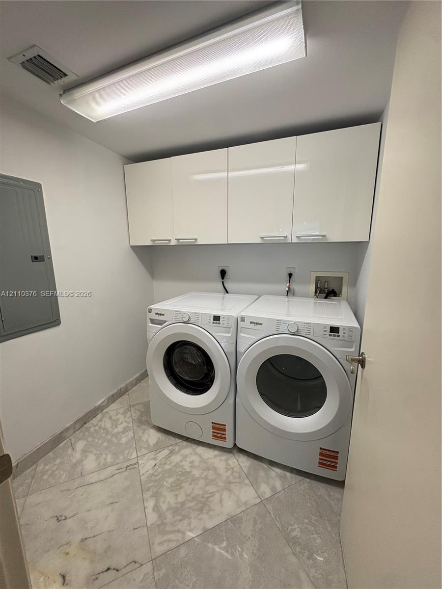 Laundry area featuring high-gloss white upper cabinetry, large-format neutral tile flooring, and integrated laundry hookups Laundry area featuring high-gloss white upper cabinetry, large-format neutral tile flooring, and integrated laundry hookups