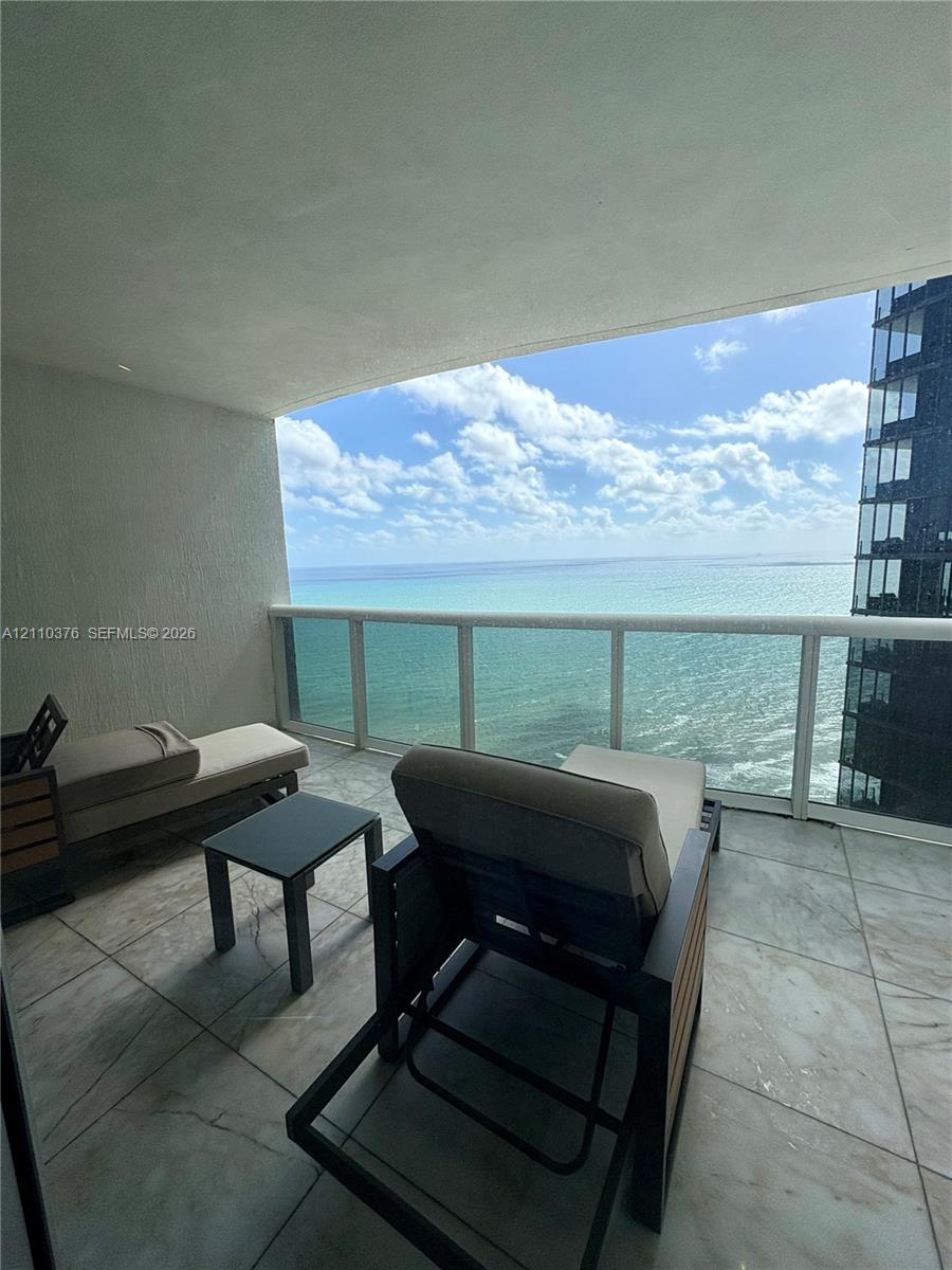 Covered balcony featuring large-format tile flooring and a glass panel railing Covered balcony featuring large-format tile flooring and a glass panel railing