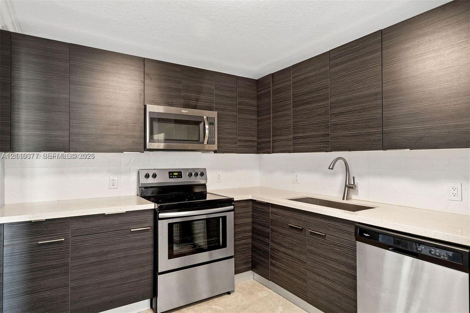 Kitchen featuring dark wood-finish cabinetry, solid surface countertops, stainless steel electric range, built-in microwave, and integrated stainless steel dishwasher Kitchen featuring dark wood-finish cabinetry, solid surface countertops, stainless steel electric range, built-in microwave, and integrated stainless steel dishwasher