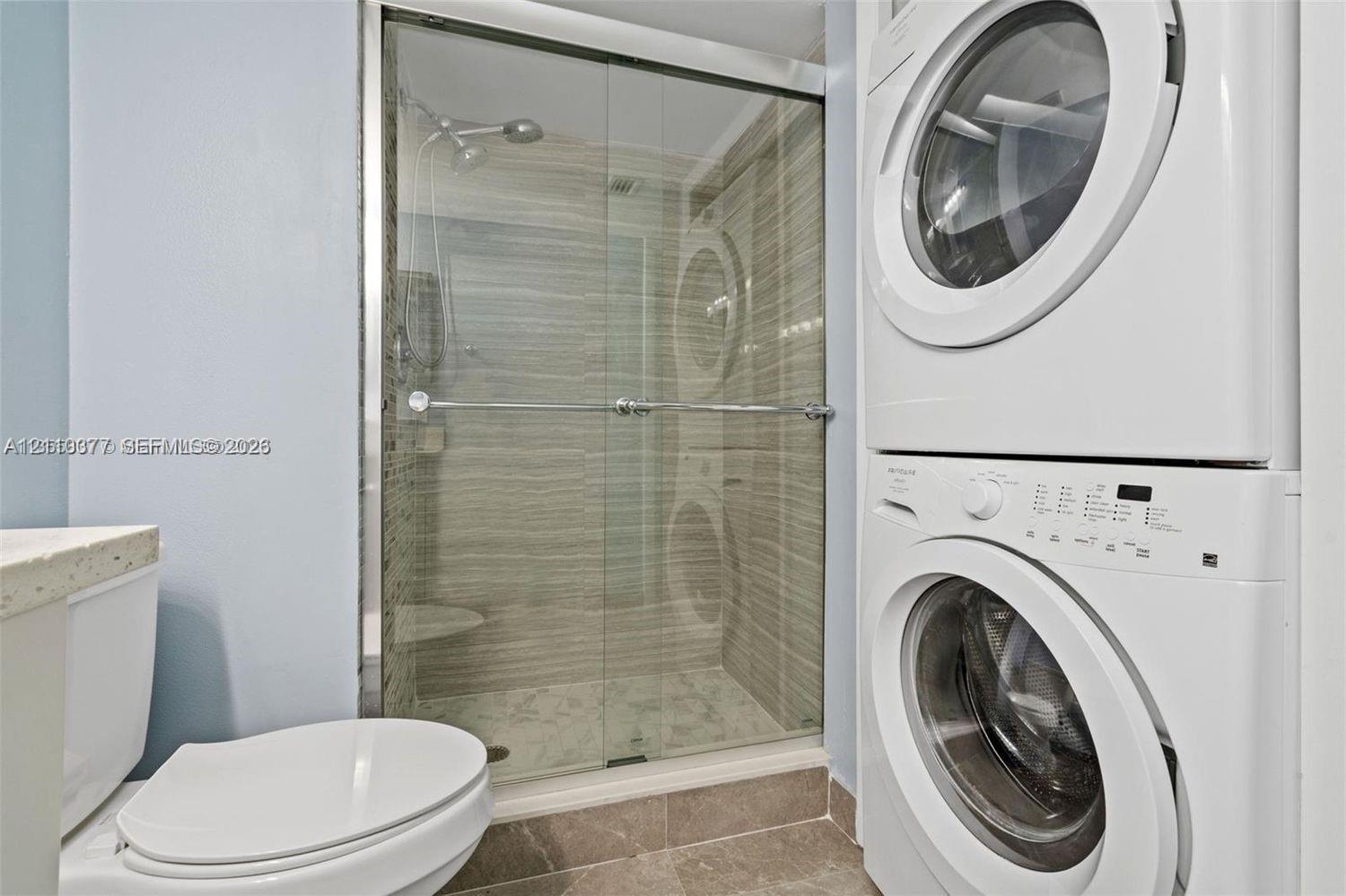 Shower with sliding glass enclosure and tiled walls, stacked washer and dryer unit, and ceramic floor tiling