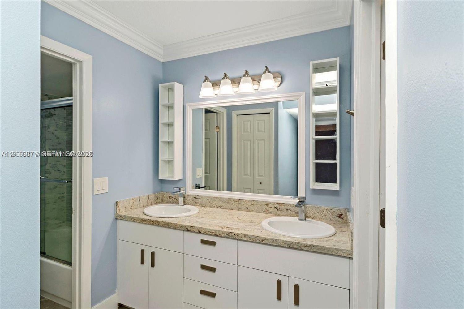 Dual-sink vanity with stone-finish countertop, white cabinetry, wall-mounted storage niches, and a four-light fixture