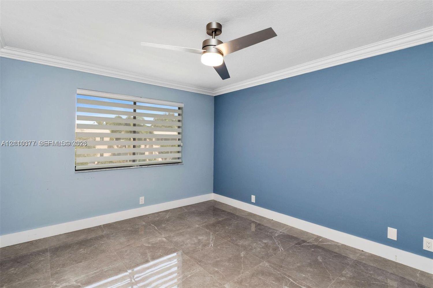 Room featuring large-format tile flooring, crown molding, a modern three-blade ceiling fan with integrated lighting, and dual-layered window shades