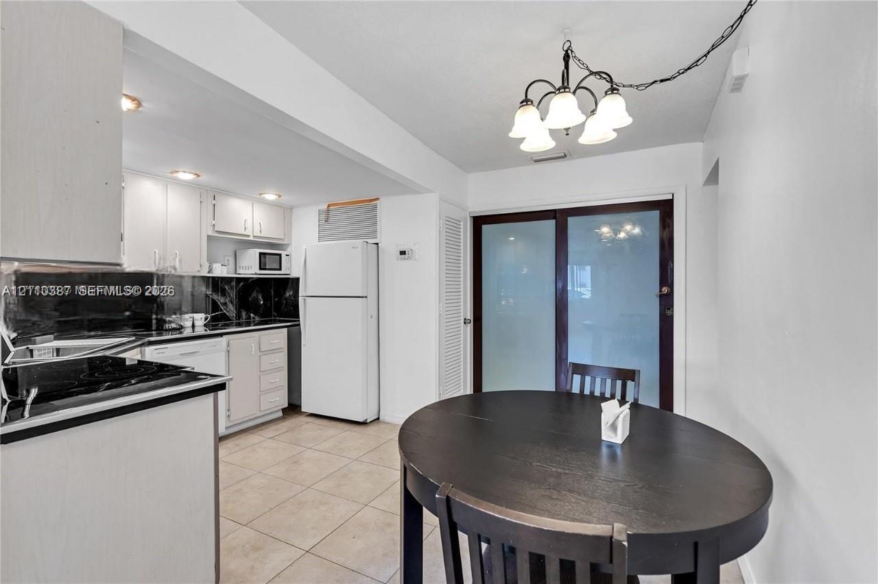 Kitchen featuring flat-panel cabinetry, dark stone-finish countertops, tile flooring, five-light chandelier, and glass-paneled sliding door Kitchen featuring flat-panel cabinetry, dark stone-finish countertops, tile flooring, five-light chandelier, and glass-paneled sliding door