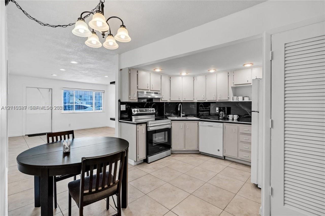 Kitchen featuring white shaker-style cabinetry, black stone countertops, stainless steel appliances, and ceramic tile flooring, complemented by a multi-light chandelier Kitchen featuring white shaker-style cabinetry, black stone countertops, stainless steel appliances, and ceramic tile flooring, complemented by a multi-light chandelier