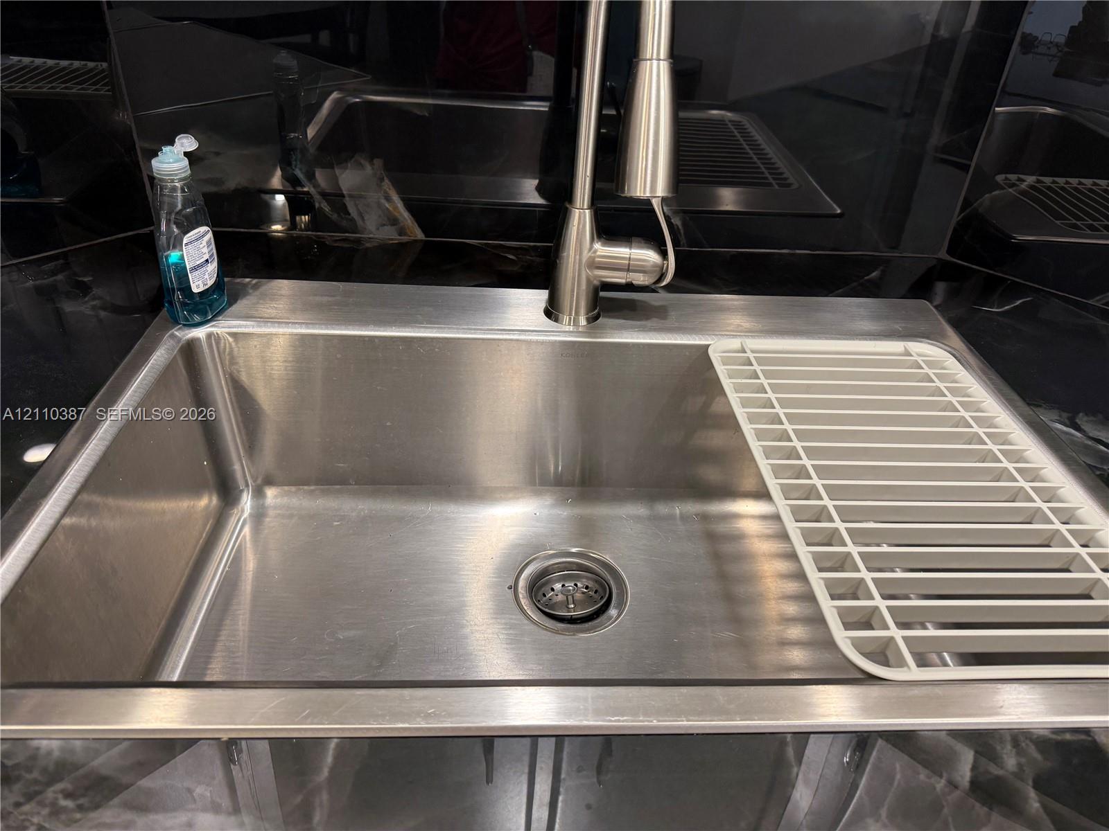 Undermount stainless steel kitchen sink featuring a high-arc pull-down faucet and dark stone-surface countertops Undermount stainless steel kitchen sink featuring a high-arc pull-down faucet and dark stone-surface countertops