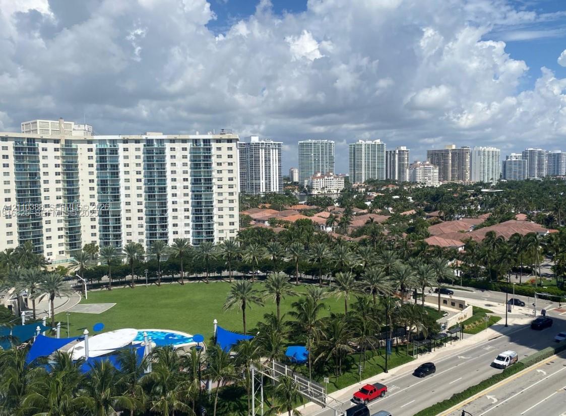 High-rise urban landscape featuring expansive green space, mature palm trees, multi-story residential structures, and blue shade structures