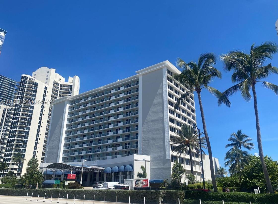 Multi-story mid-rise exterior featuring a concrete faade, private balconies, an arched entrance portico, and mature palm trees