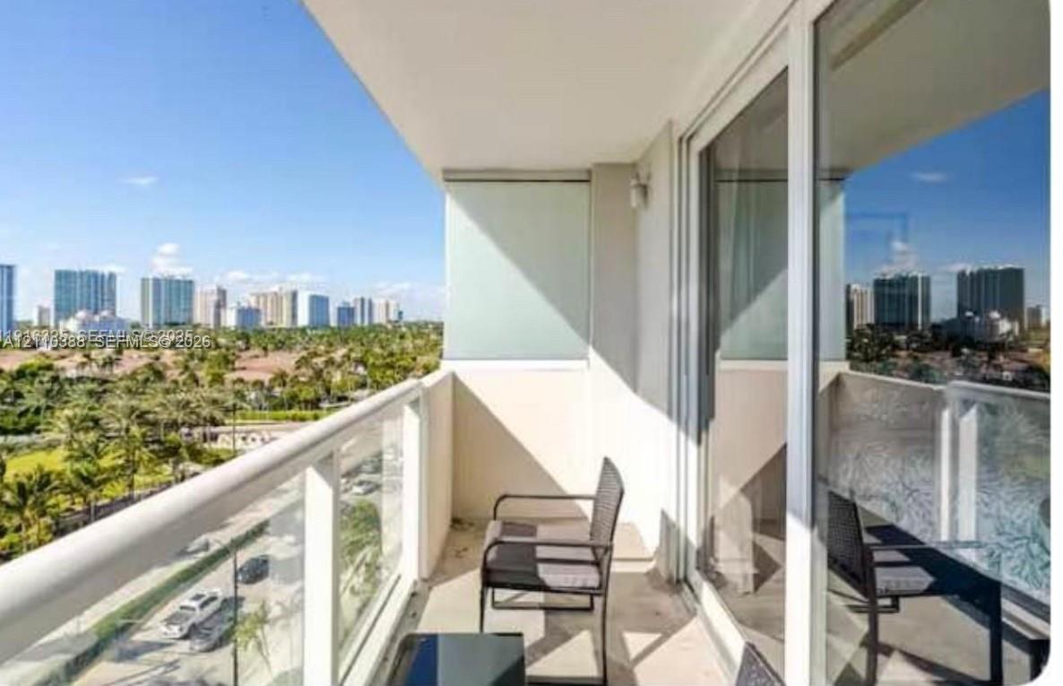 Covered balcony featuring a glass-panel railing, expansive sliding glass doors, and a panoramic perspective of the cityscape and surrounding greenery Covered balcony featuring a glass-panel railing, expansive sliding glass doors, and a panoramic perspective of the cityscape and surrounding greenery