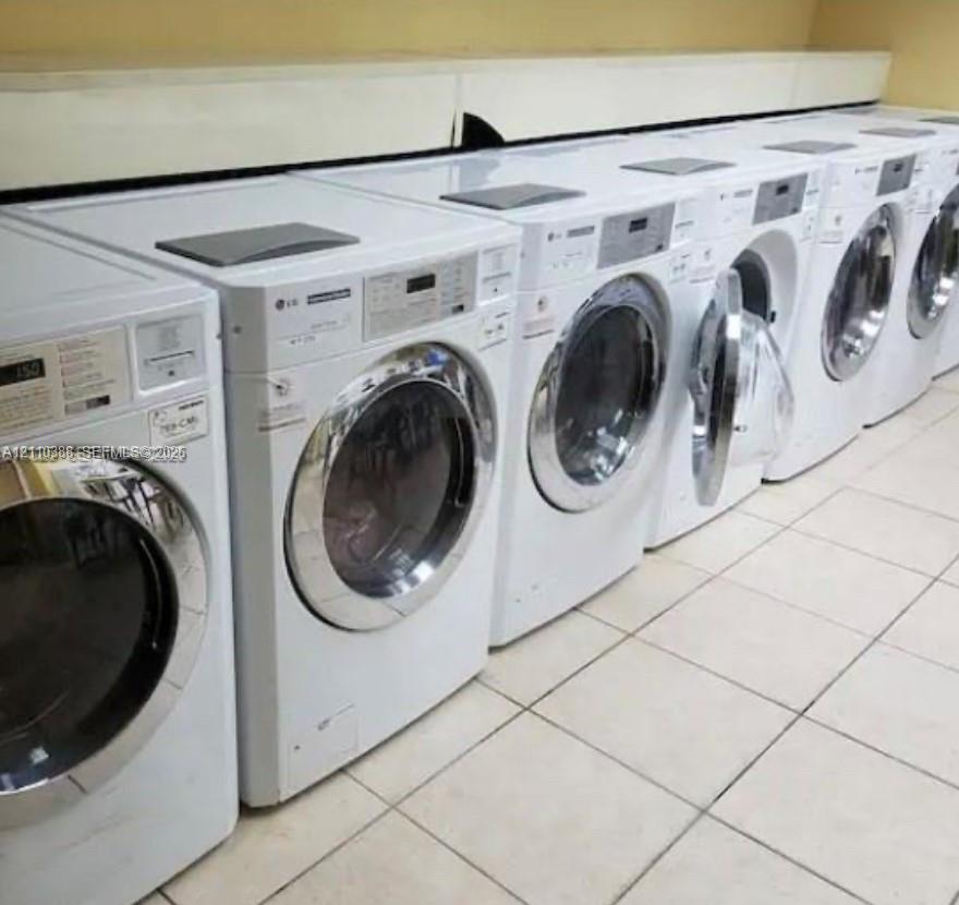 Utility area featuring a row of white front-loading washing machines with chrome-finished doors and white tile flooring
