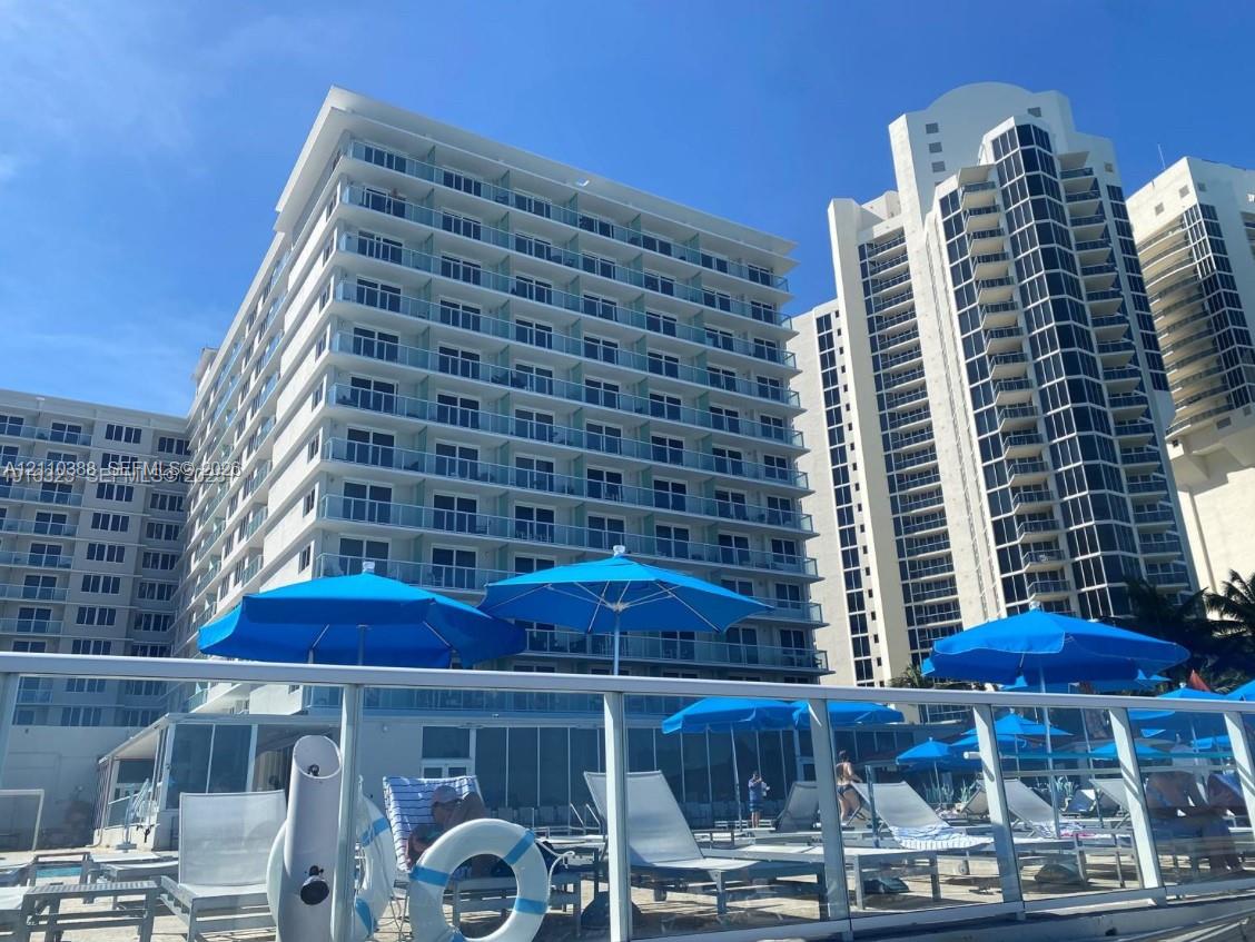High-rise residential exterior featuring expansive glass-railed balconies, a multi-story concrete facade, and a ground-level swimming pool deck High-rise residential exterior featuring expansive glass-railed balconies, a multi-story concrete facade, and a ground-level swimming pool deck