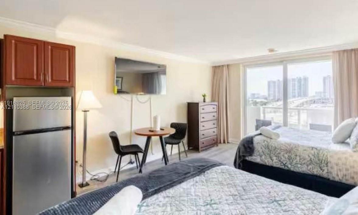Studio featuring wood-finish flooring, a stainless steel refrigerator, dark wood-finish cabinetry, and glass sliding doors providing exterior exposure Studio featuring wood-finish flooring, a stainless steel refrigerator, dark wood-finish cabinetry, and glass sliding doors providing exterior exposure