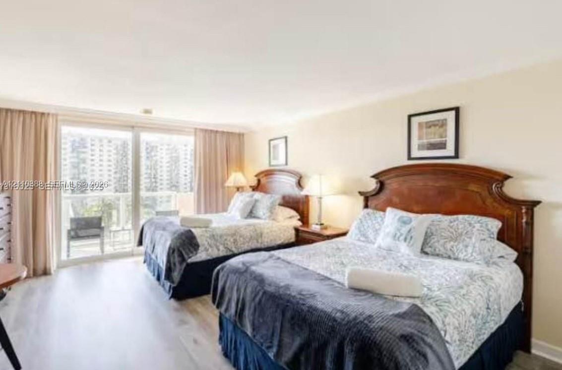 Neutral-toned bedroom featuring wood-finish flooring, floor-to-ceiling drapery, and sliding glass doors providing outdoor access Neutral-toned bedroom featuring wood-finish flooring, floor-to-ceiling drapery, and sliding glass doors providing outdoor access
