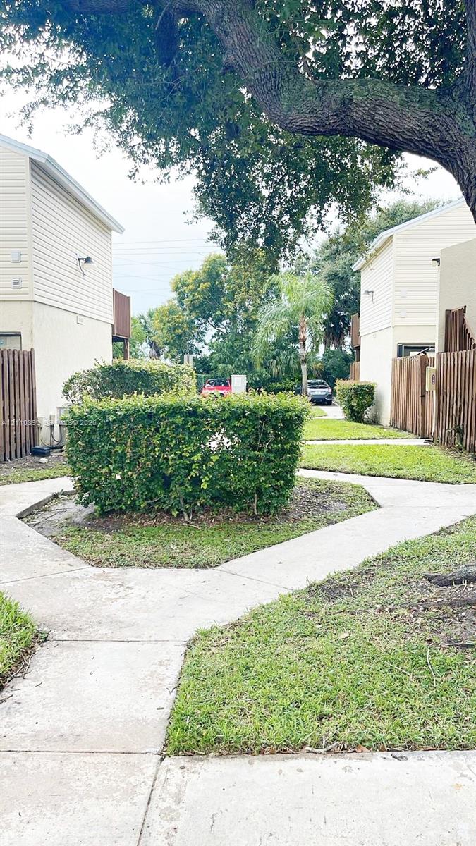 Exterior grounds featuring concrete walkways, manicured landscaping, mature trees, and wooden fencing Exterior grounds featuring concrete walkways, manicured landscaping, mature trees, and wooden fencing