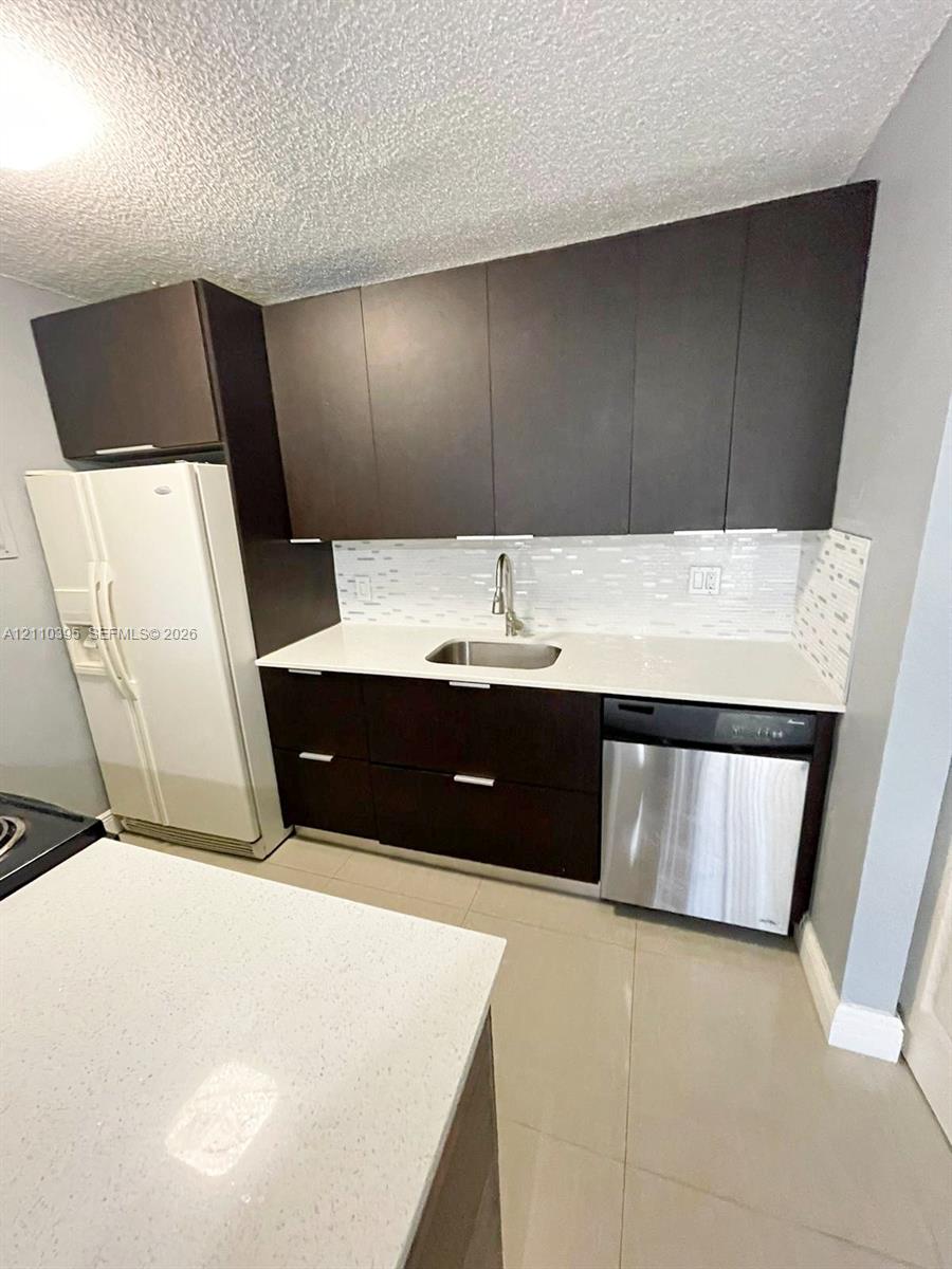 Dark-toned cabinetry featuring flat-panel doors, quartz countertops, stainless steel undermount sink with arched faucet, mosaic tile backsplash, and stainless steel dishwasher Dark-toned cabinetry featuring flat-panel doors, quartz countertops, stainless steel undermount sink with arched faucet, mosaic tile backsplash, and stainless steel dishwasher