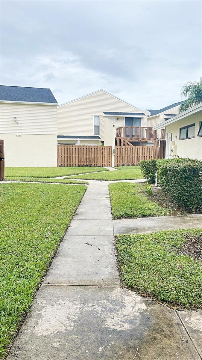 Exterior area featuring a paved walkway, manicured lawn, wood privacy fencing, and second-story wood balcony Exterior area featuring a paved walkway, manicured lawn, wood privacy fencing, and second-story wood balcony