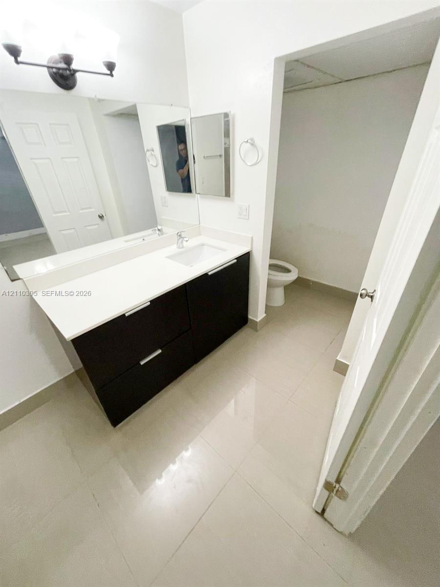 Floating vanity featuring a dark-toned cabinet, integrated countertop with a rectangular basin, large wall-mounted mirror, three-light fixture, and ceramic tile flooring