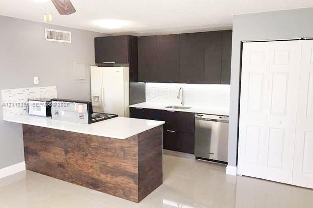 Kitchen featuring dark cabinetry, white countertops, stainless steel dishwasher, tile backsplash, and wood-finish breakfast bar Kitchen featuring dark cabinetry, white countertops, stainless steel dishwasher, tile backsplash, and wood-finish breakfast bar