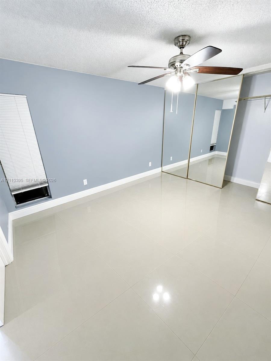 Room featuring large-format tile flooring, mirrored closet doors, a ceiling fan with integrated light fixture, and a window with horizontal blinds