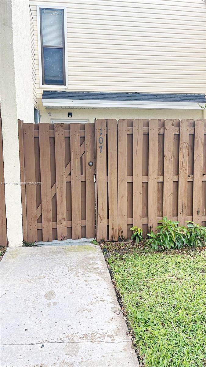 Exterior entrance featuring a private wooden privacy fence, a gated entry, a concrete walkway, and beige horizontal siding Exterior entrance featuring a private wooden privacy fence, a gated entry, a concrete walkway, and beige horizontal siding