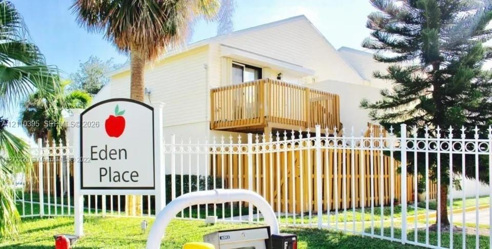 Multi-story building with light-colored siding, wood-railing balcony, and perimeter white metal fencing