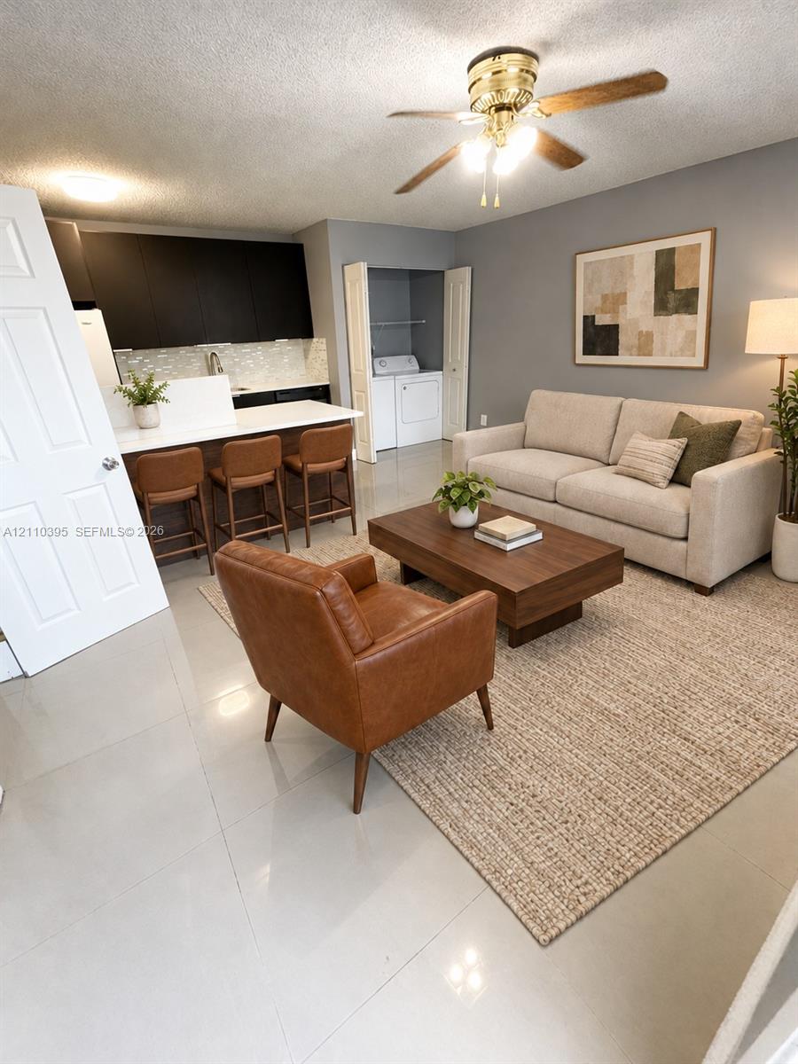 Open-concept living space featuring high-gloss, dark-toned cabinetry, quartz countertops, tile flooring, and an integrated laundry closet with bifold doors
