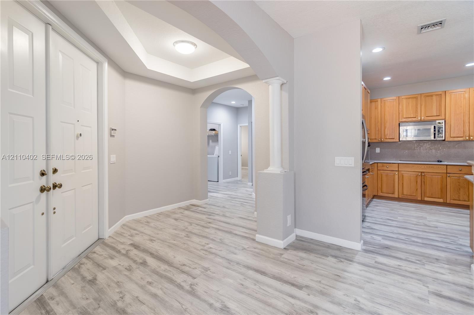 Tray ceiling with recessed lighting, arched wall opening with decorative column, and wood-finish flooring