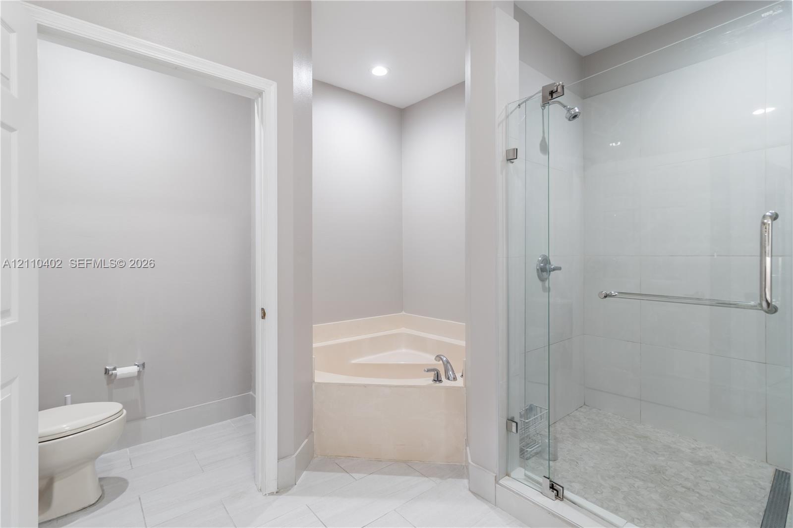 Bathroom featuring a corner soaking tub, glass-enclosed shower with tile surround, tile flooring, and a dedicated water closet